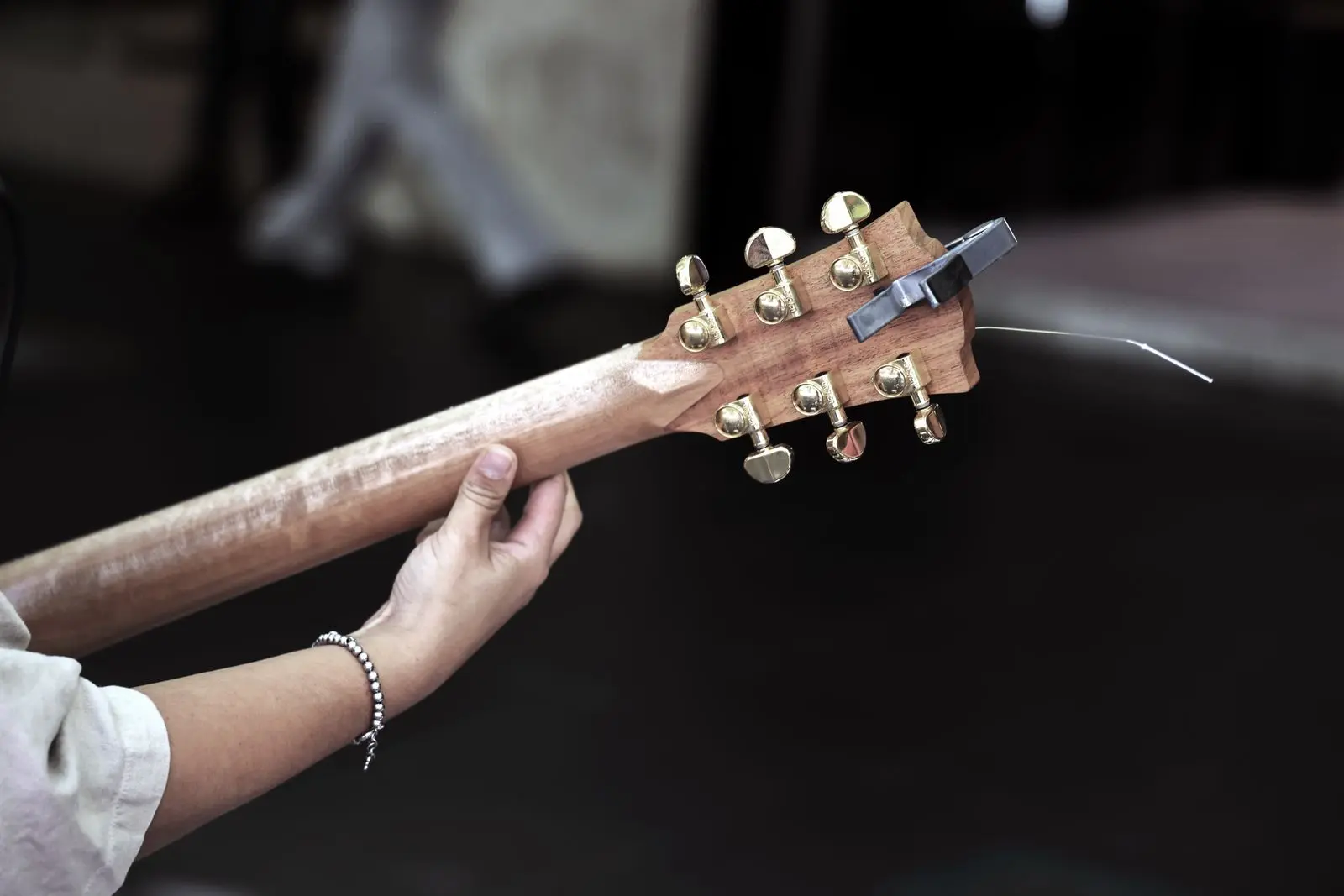 A hand on an acoustic guitar's neck, with a clip-on tuner and gold tuning pegs on the headstock
