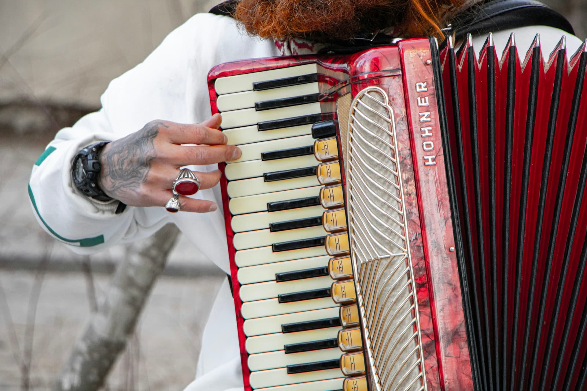 A player's hand on the keys of a red Hohner piano accordion.