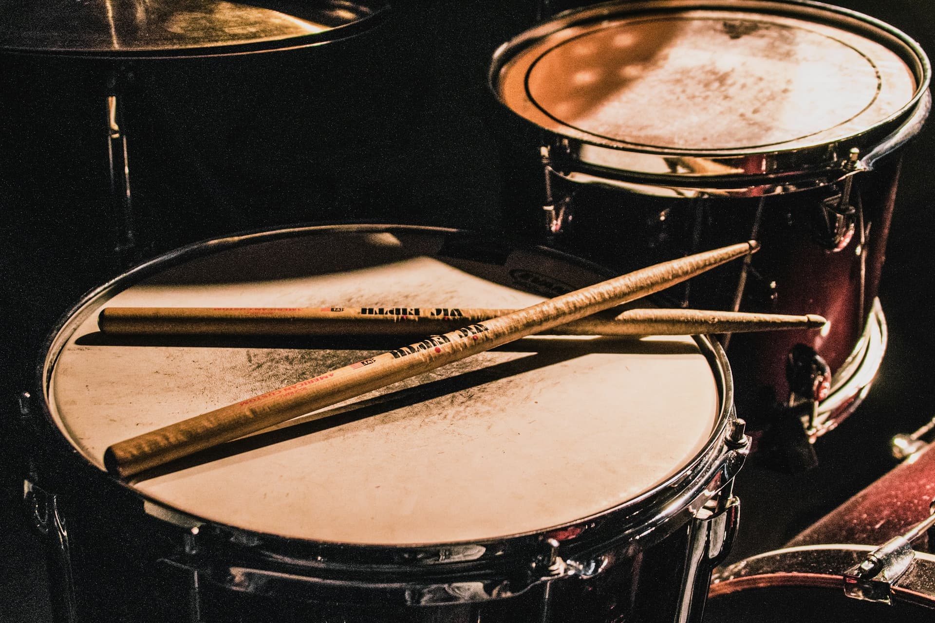 Drumsticks resting on a drum kit in warm stage light.