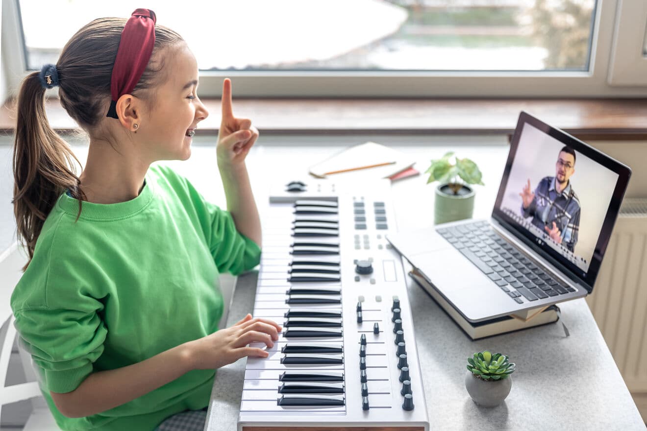 A girl learning piano with her teacher in an online lesson.
