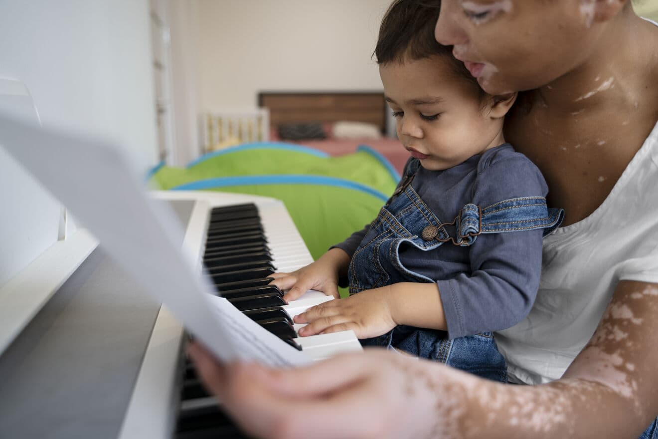 A parent and child playing piano together at home.
