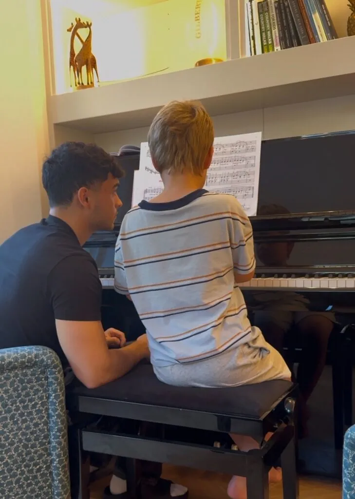 A piano teacher beside a young pupil at an upright piano.