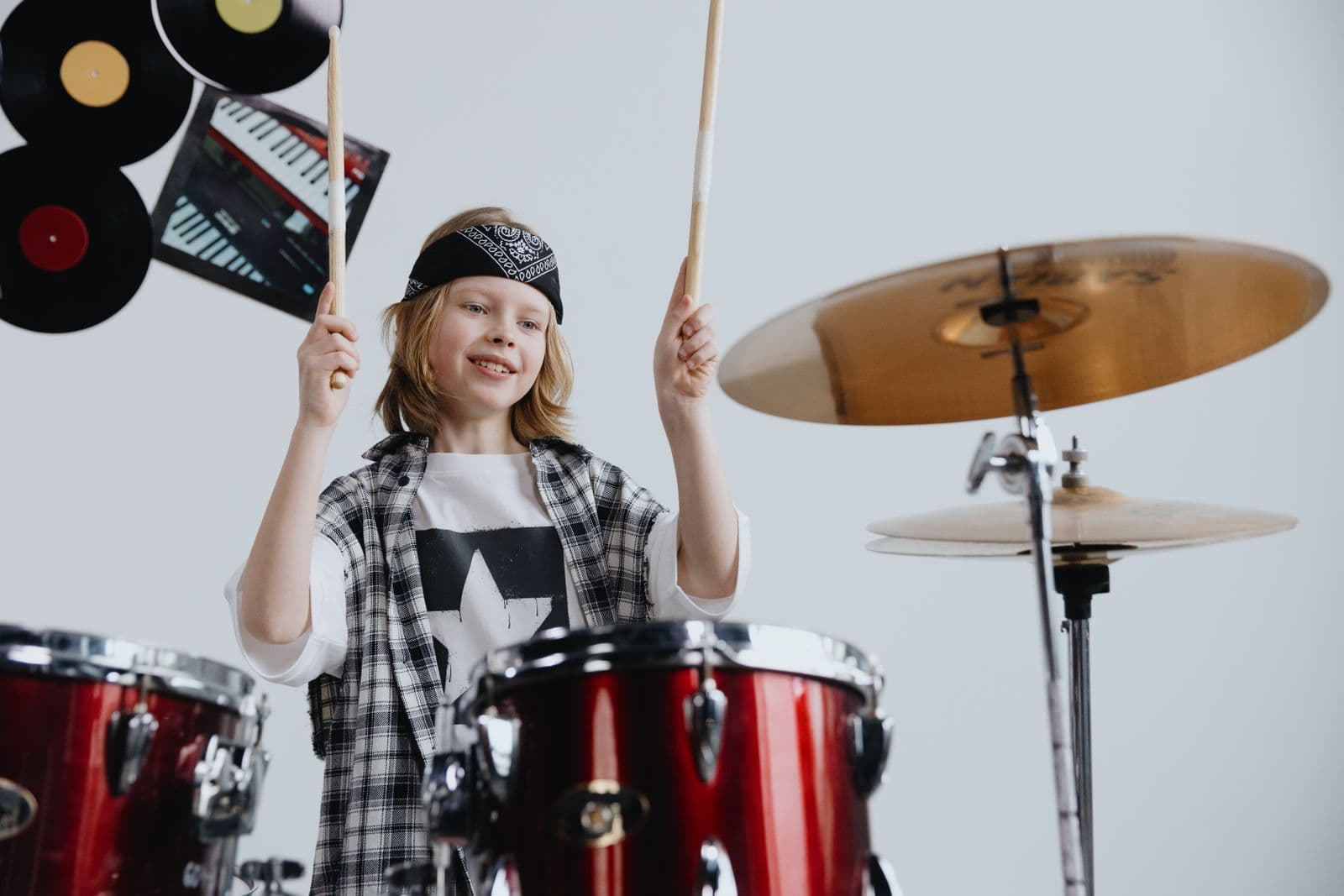 A young drummer mid-beat at a red drum kit, sticks raised.