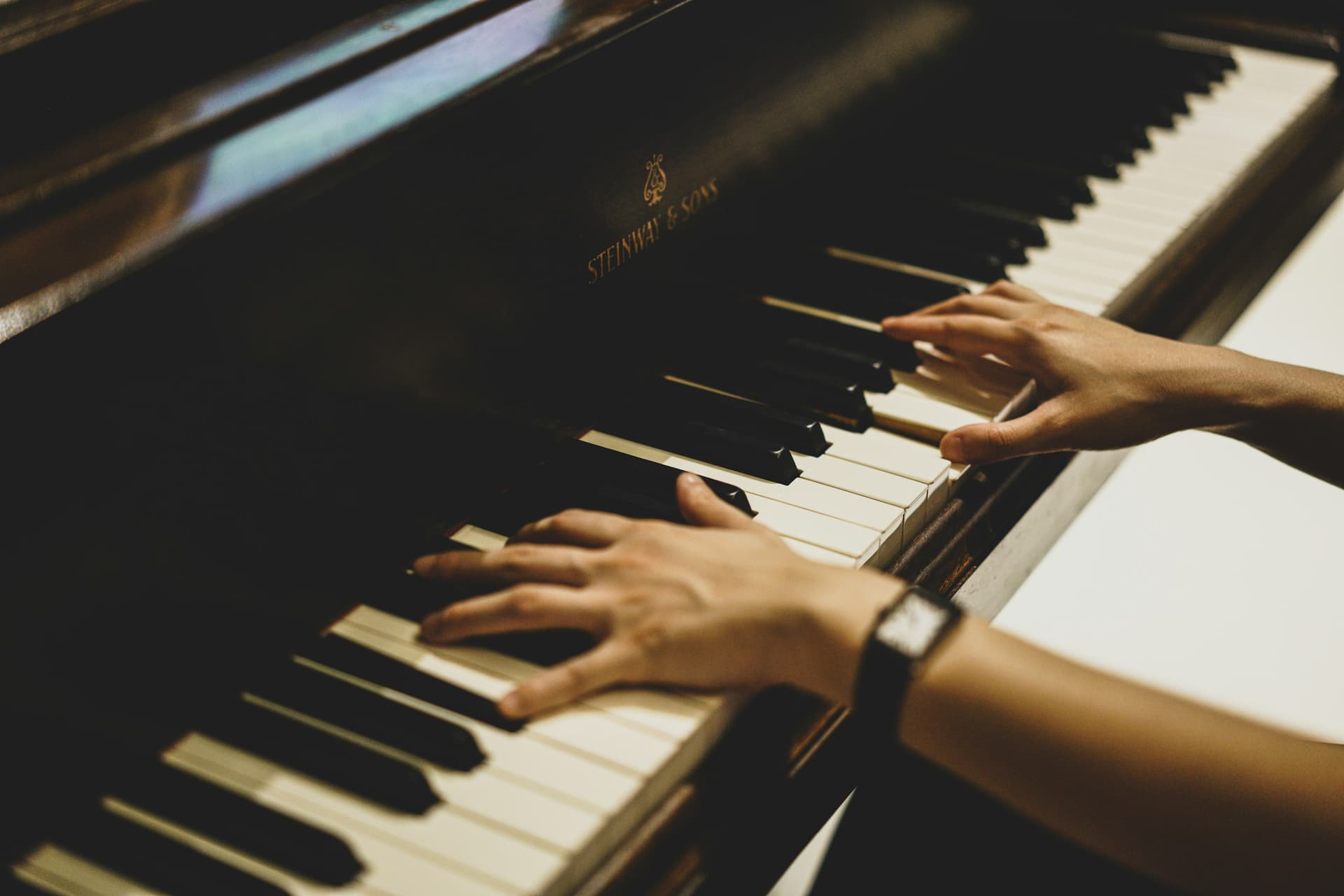 Close-up of hands playing piano keys in warm light.