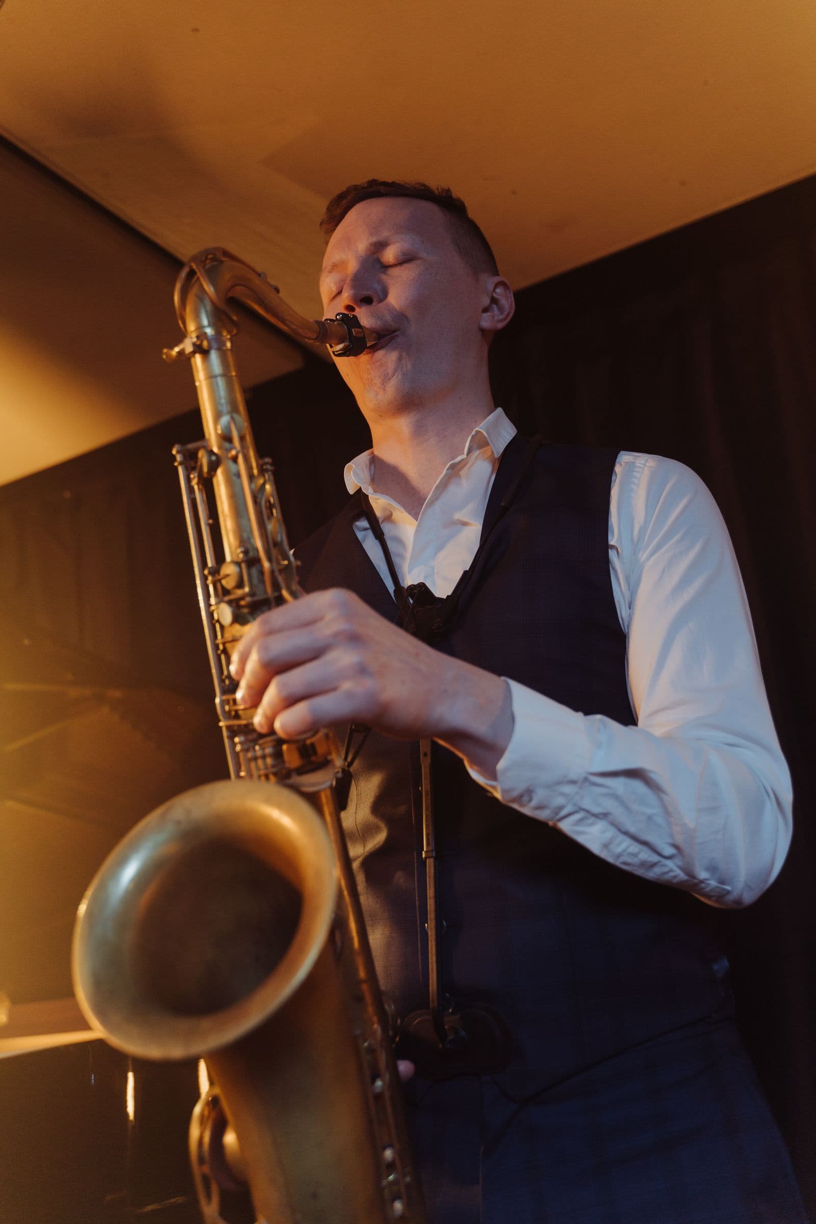 A saxophonist playing a tenor saxophone in warm amber light.