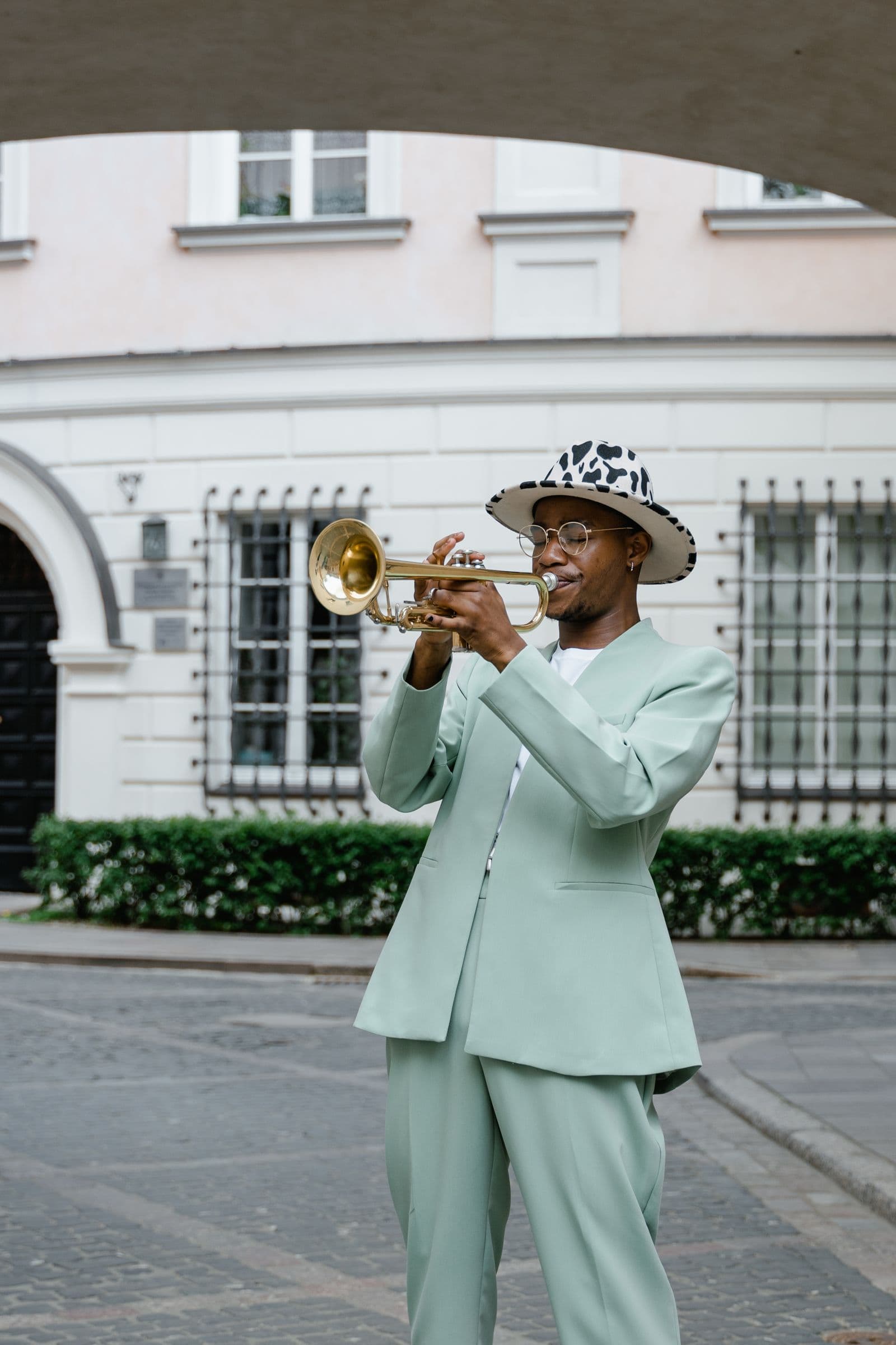 A trumpeter in a mint-green suit playing on a city street.