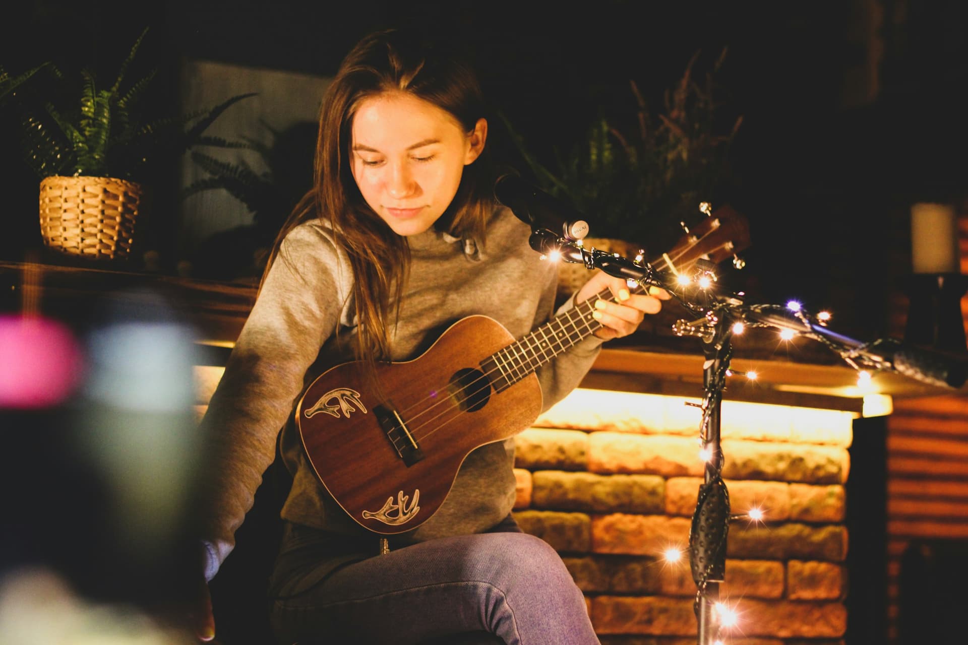 A woman seated playing the ukulele.