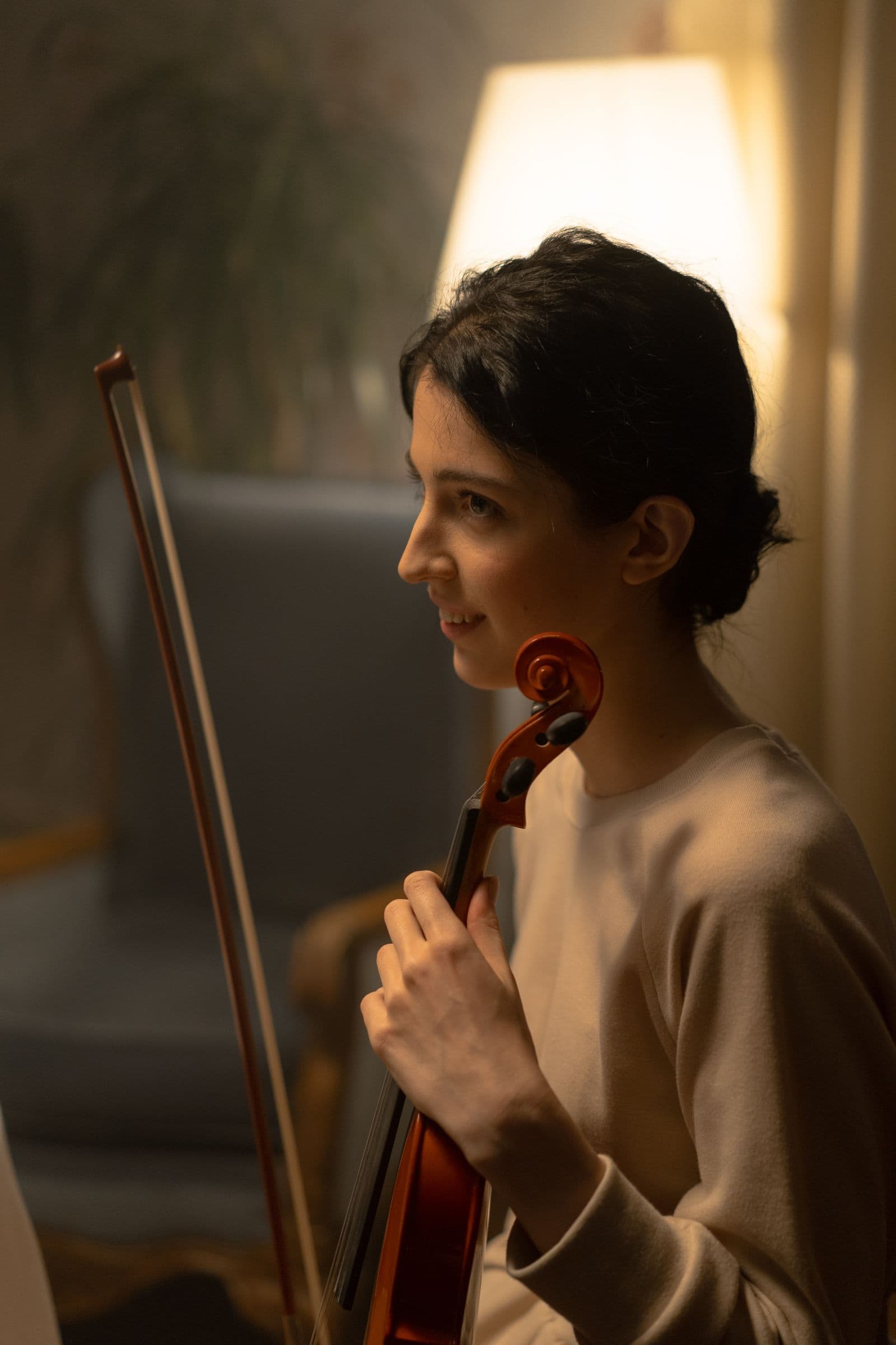 A string player seated with her instrument in warm lamp light.