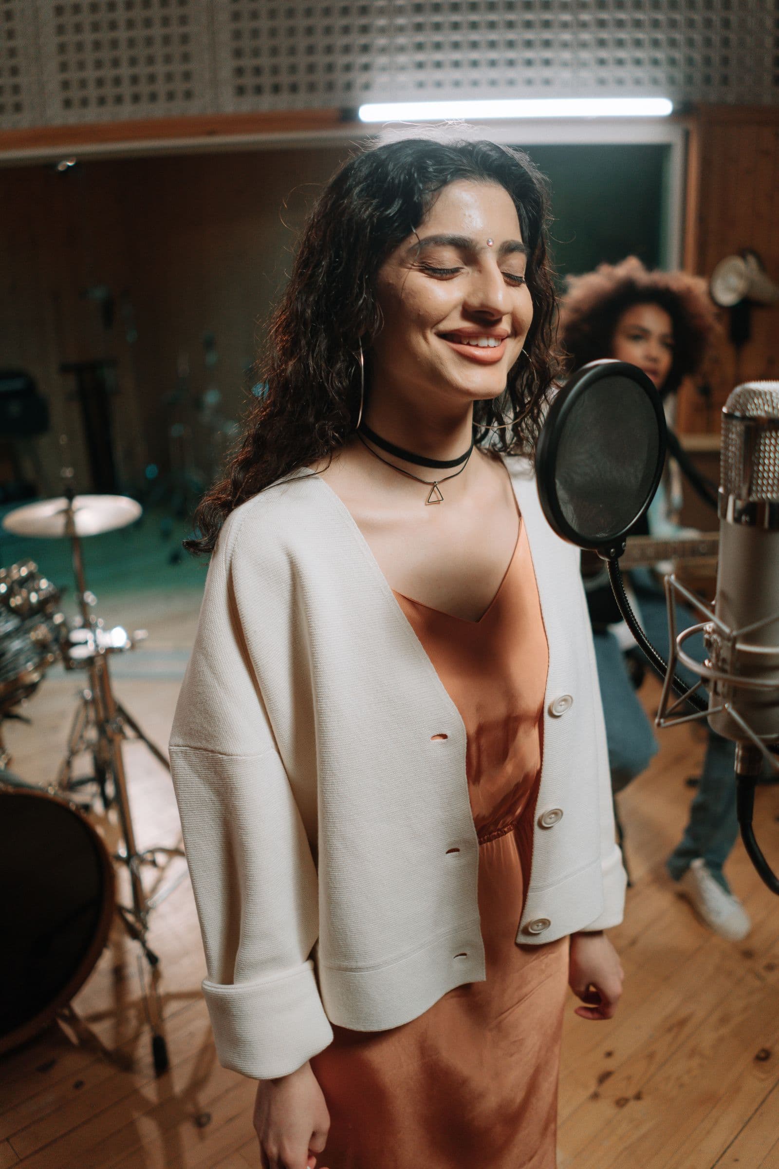 A vocalist singing at a studio microphone during a session in a warm rehearsal room.
