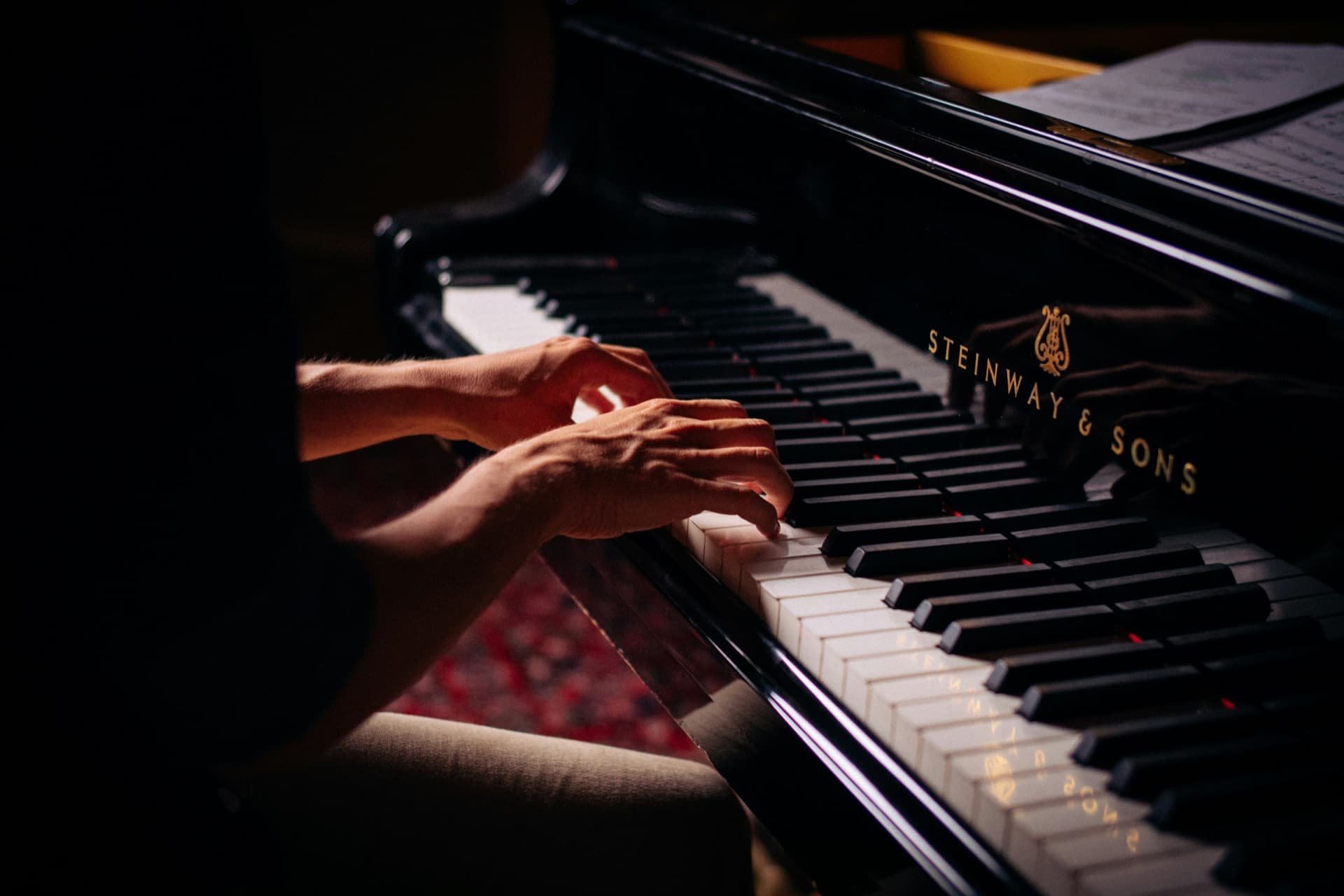 Hands playing a grand piano in warm low light.