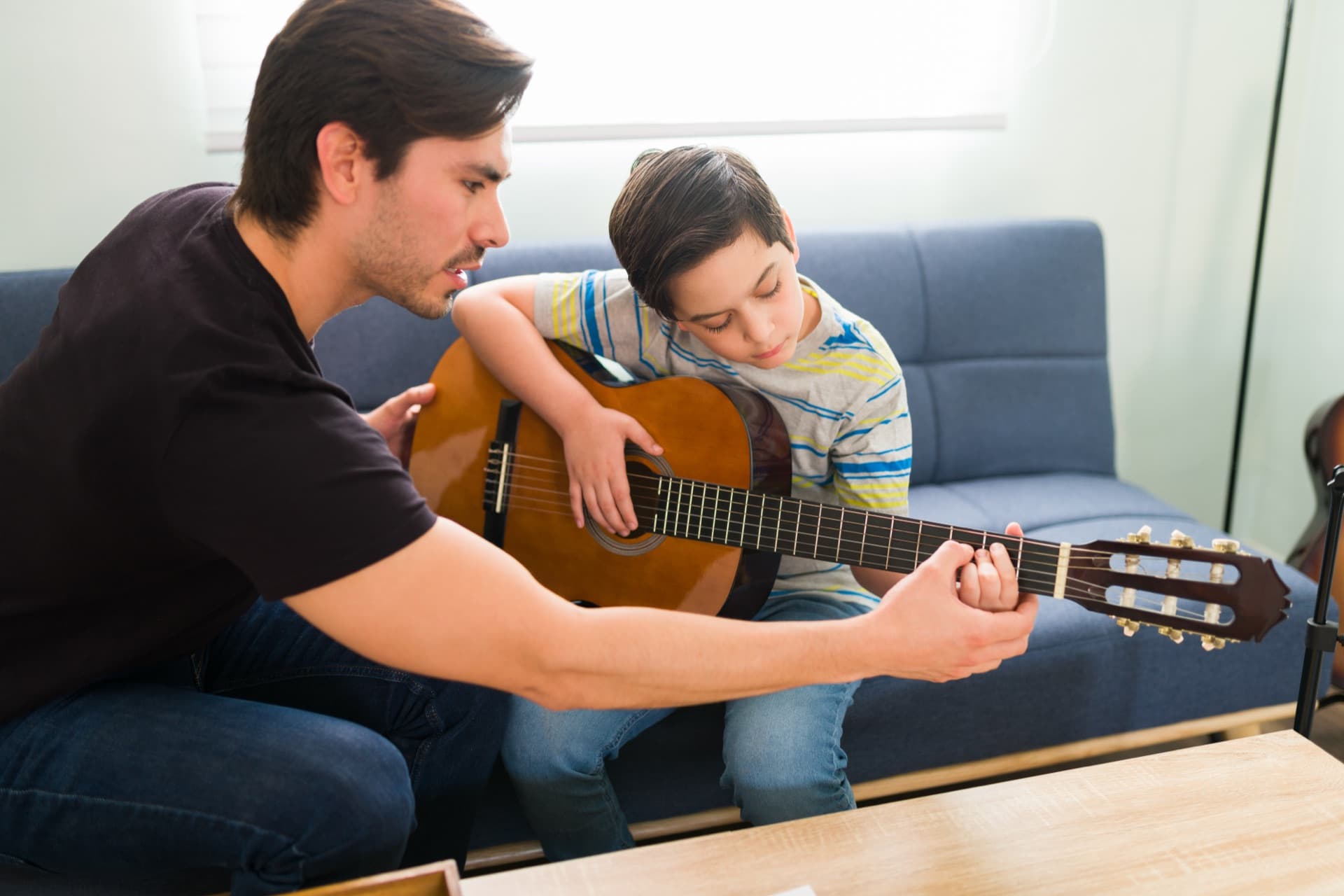 A guitar teacher shaping a young student's chord hand during a home lesson.