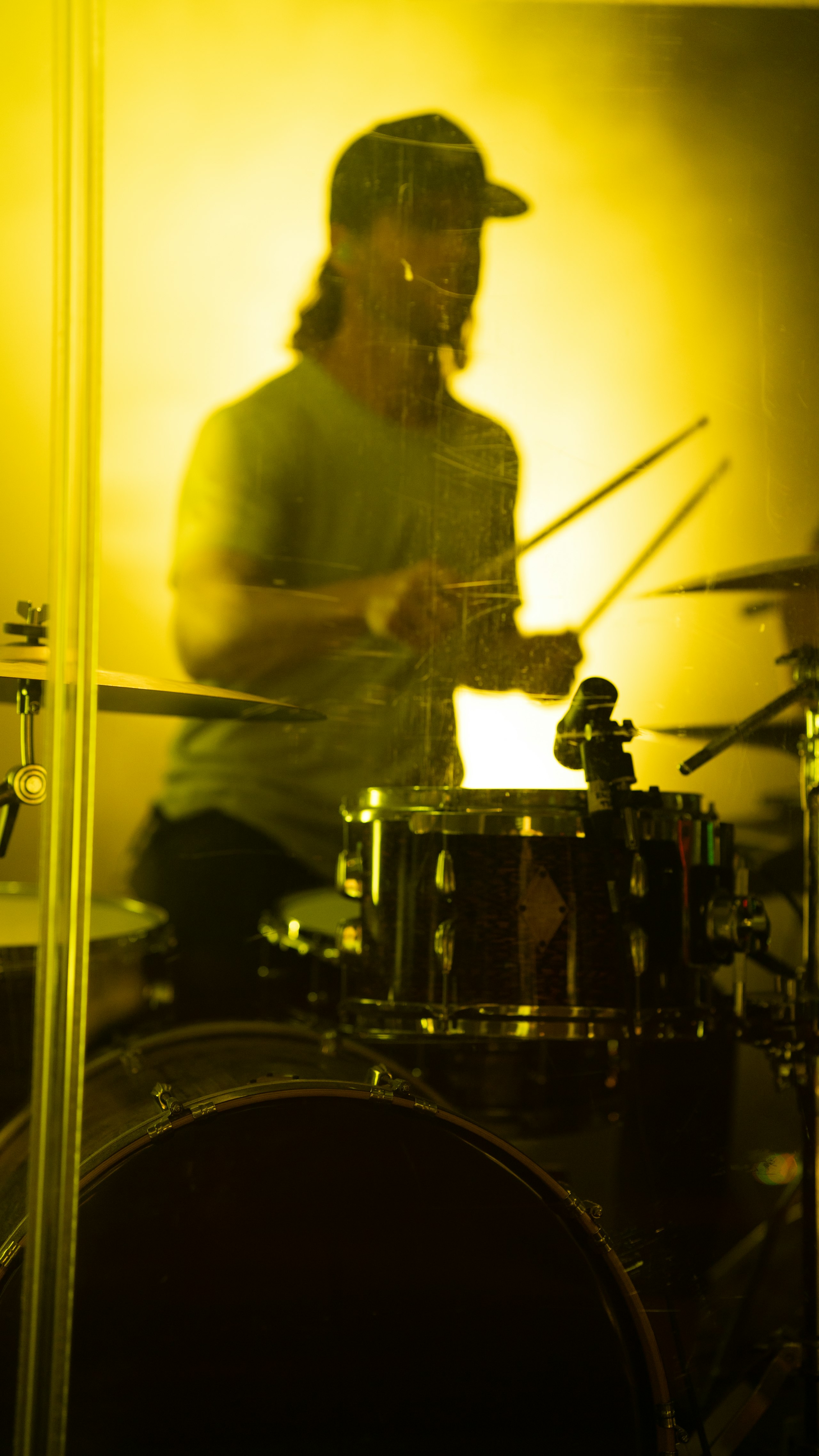 A drummer performing on a stage washed in yellow light.